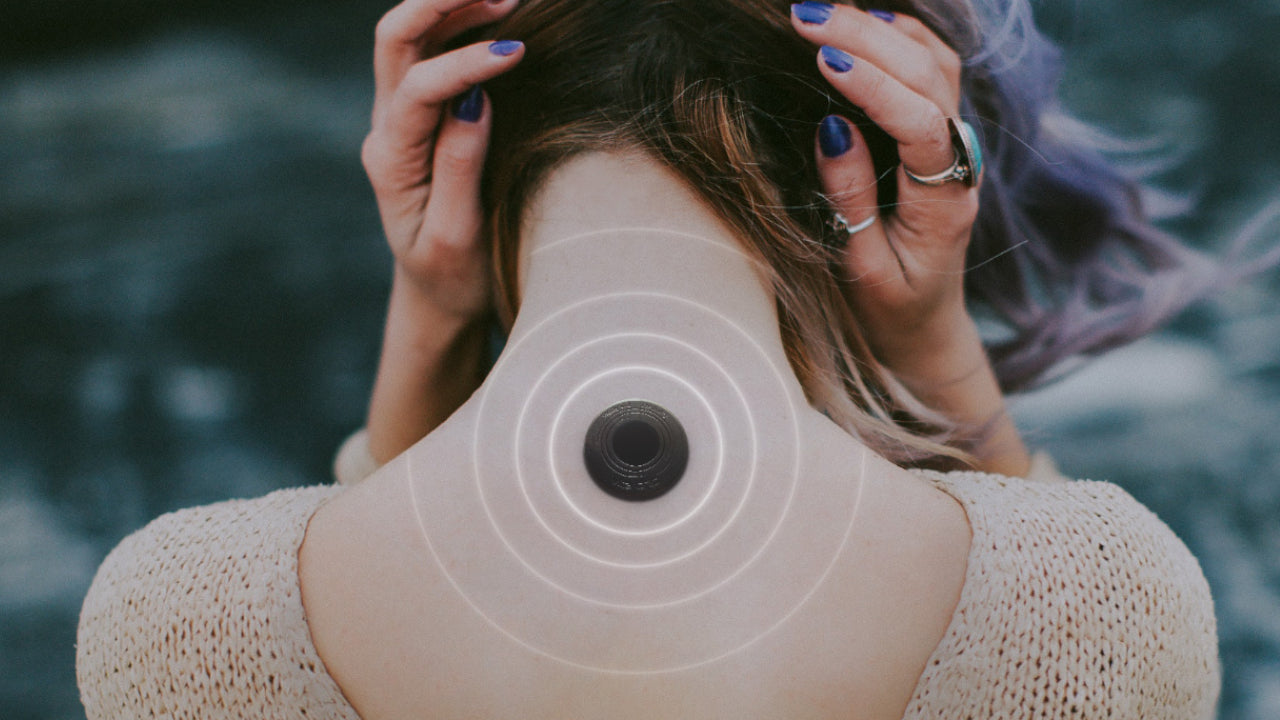 Der Nacken einer Frau, die ihre Haare zu beiden Seiten teilt. In der Mitte ihres Nackens befindet sich ein Vita Chip Health+, aus dem weiße kreisförmige Energie nach außen strahlt.